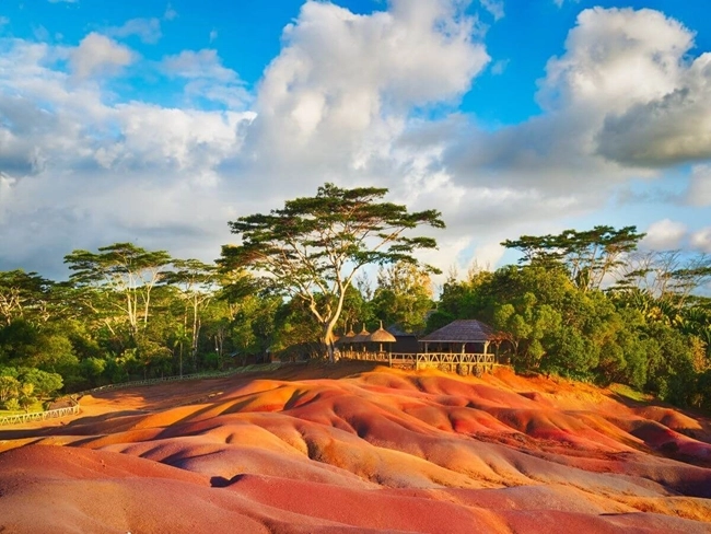 Ett landskap på Mauritius med träd och röd sand runt ett hus