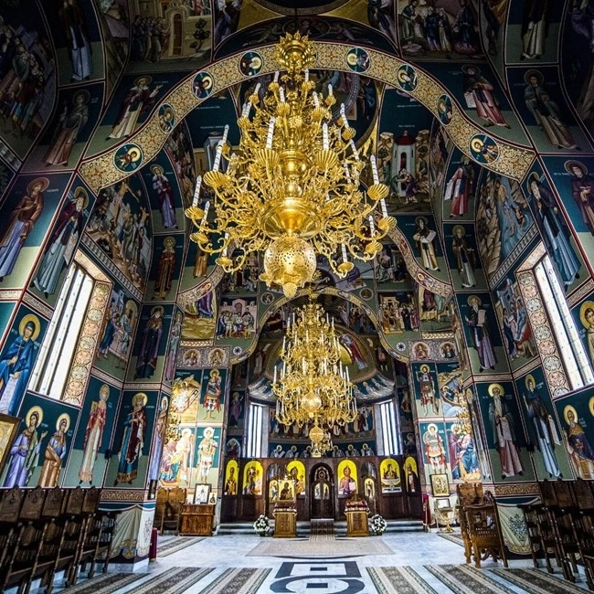 Interiören i en ortodox kyrka i Rumänien täckt av ikoner på väggar och tak, med en stor förgylld ljuskrona.