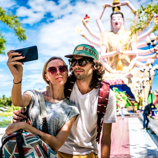 Ett par tar en selfie framför en staty av en gudom i Thailand