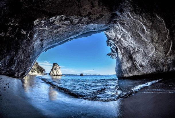 En naturskön vy inifrån en grotta, med stranden och havet utanför, inramat av klippiga grottväggar.