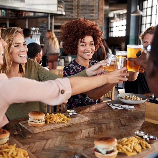 En grupp vänner skålar och äter en hamburgare med pommes frites på en restaurang