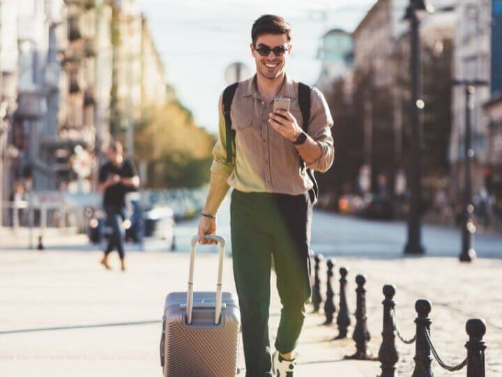 en man som går med en resväska och ler medan han tittar på sin smartphone